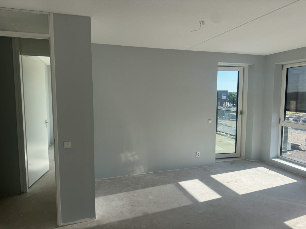 Nieuw appartement met kale wanden, een betonvloer en een deur naar het balkon, klaar voor de afwerking